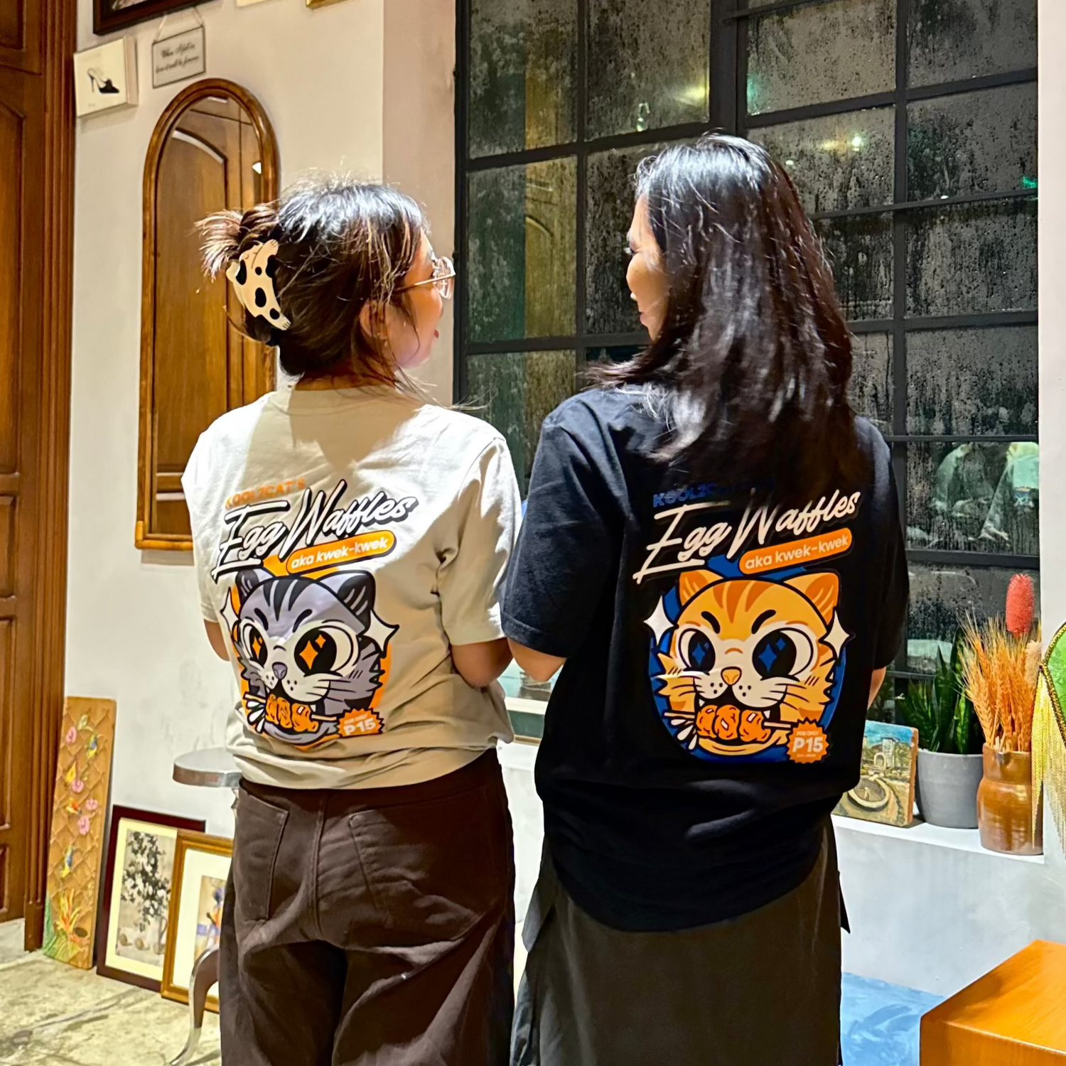 Two people wearing cat t-shirts with cartoon designs standing in a room.